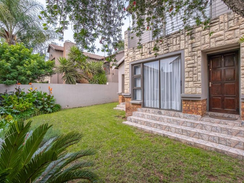 Rear view of the property featuring stone and brick facade, tiled entrance steps, sliding glass doors, and a well-maintained private garden.