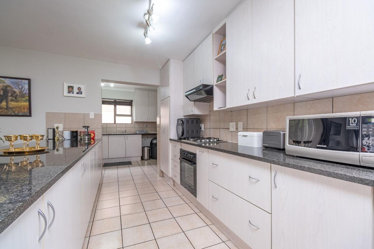 A functional kitchen featuring light-toned cabinetry, granite countertops, a built-in oven with gas hob, and tiled flooring, with an adjacent scullery area.