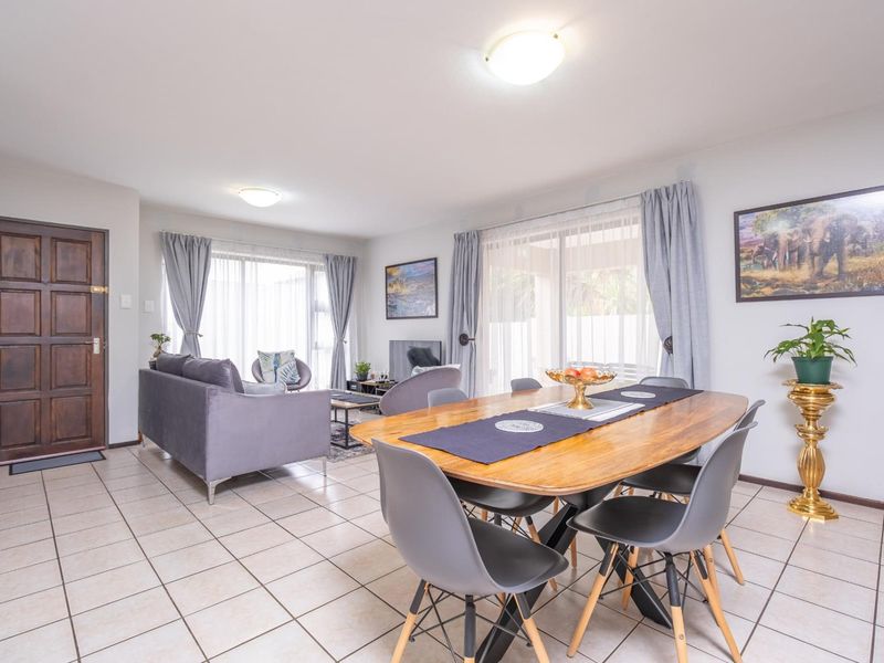 Spacious open-plan living and dining area featuring neutral tiled flooring, abundant natural light through sliding glass doors, and a solid wood entrance door.