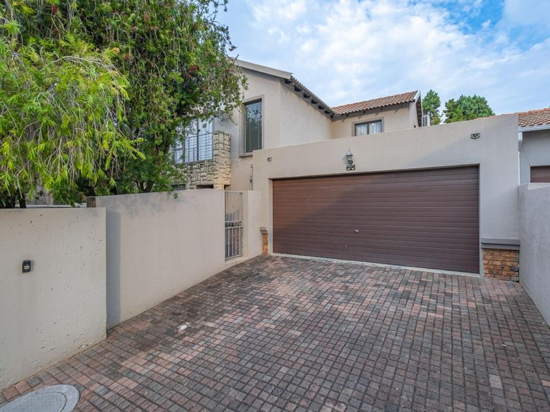 Front elevation of the property featuring a paved driveway, double garage, and secure boundary wall with gated access.