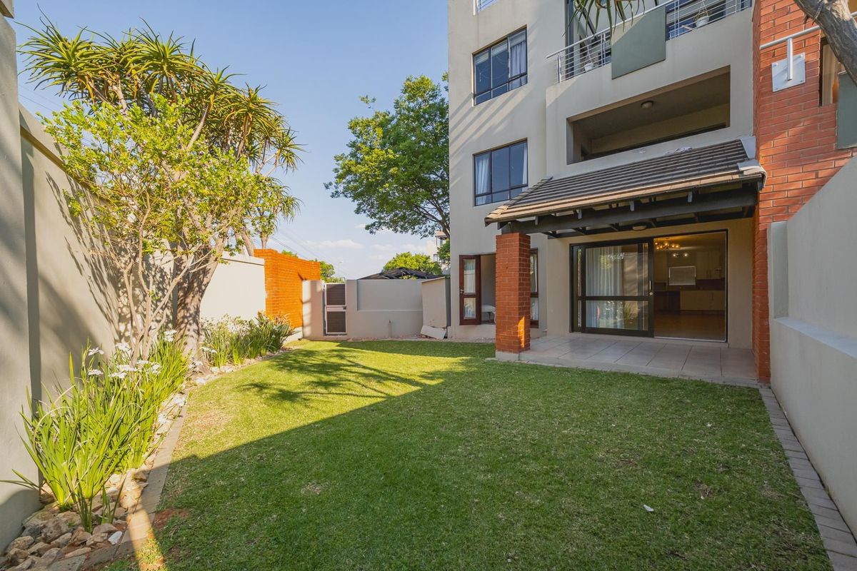 A private rear garden featuring a well-maintained lawn, a covered patio area with brick pillars, and direct access to the apartment interior.