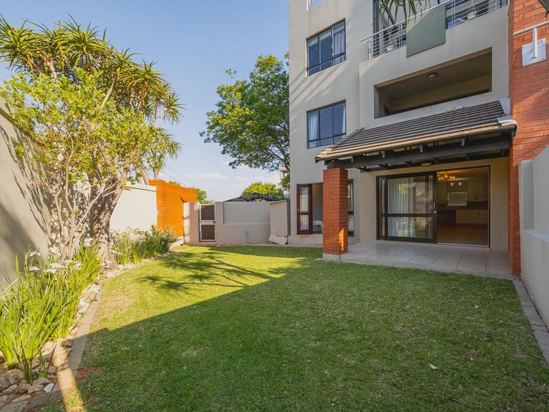 A private rear garden featuring a well-maintained lawn, a covered patio area with brick pillars, and direct access to the apartment interior.