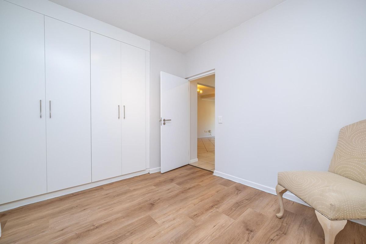 A bright, neutral bedroom featuring modern laminate flooring and ample built-in cupboard storage space.