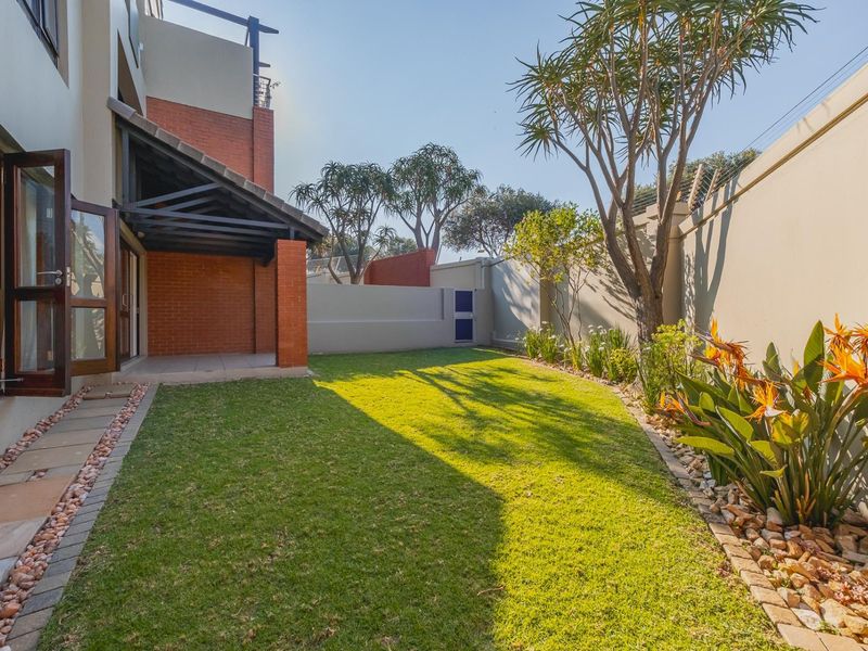 A well-maintained rear garden featuring a covered patio, manicured lawn, paved pathways, and secure perimeter walls with electric fencing.
