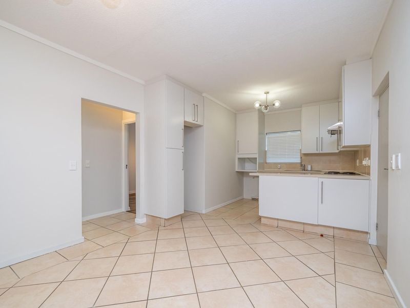 Open-plan kitchen area featuring white built-in cabinetry, tiled flooring, and a functional layout with integrated hob and extractor fan.