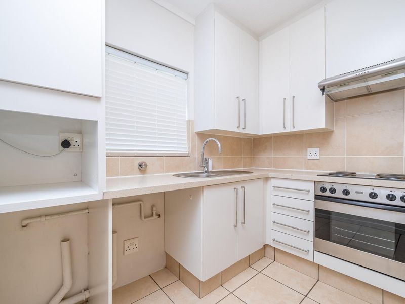 A clean, functional kitchen featuring white cabinetry, tiled backsplash, built-in oven with hob, extractor fan, and dedicated space for under-counter appliances.