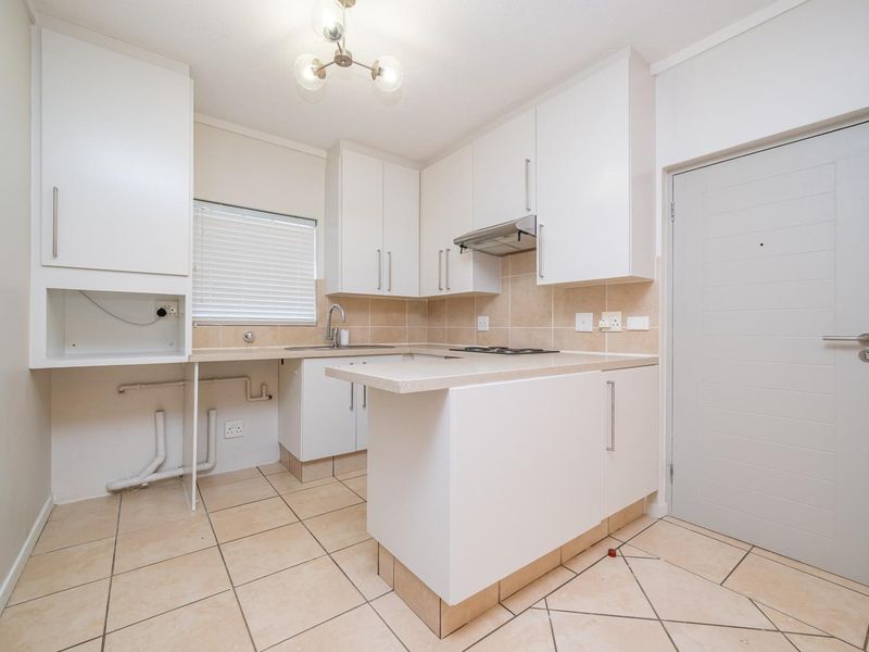 A clean, functional kitchen featuring white cabinetry, stone countertops, a built-in hob, extractor fan, and tiled flooring with an adjacent service door.