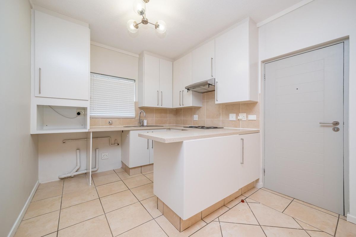 A clean, functional kitchen featuring white cabinetry, stone countertops, a built-in hob, extractor fan, and tiled flooring with an adjacent service door.