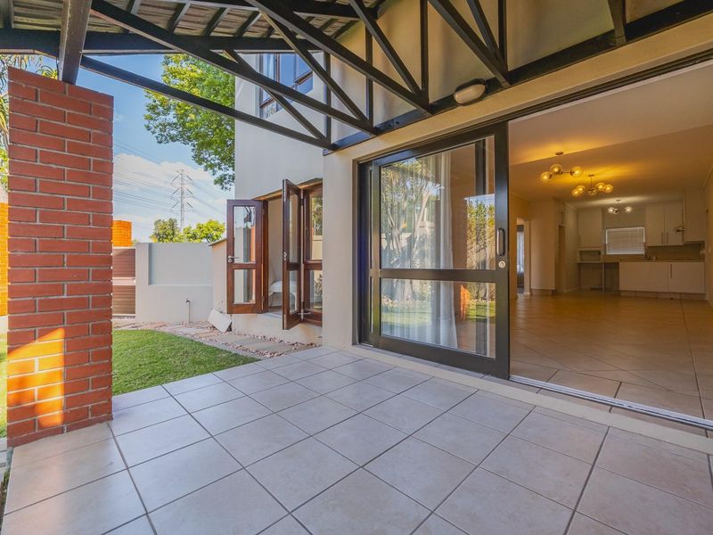 A covered patio area with tiled flooring and exposed steel trusses, providing seamless indoor-outdoor flow through large sliding glass doors to the garden.