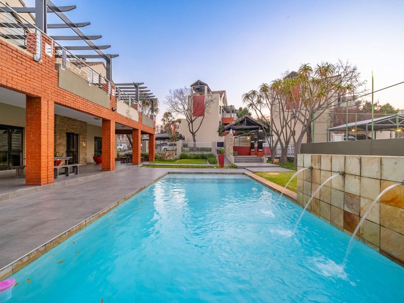 A well-maintained communal pool area featuring a stone-clad water feature, tiled patio space, and brick architectural detailing within an apartment complex.