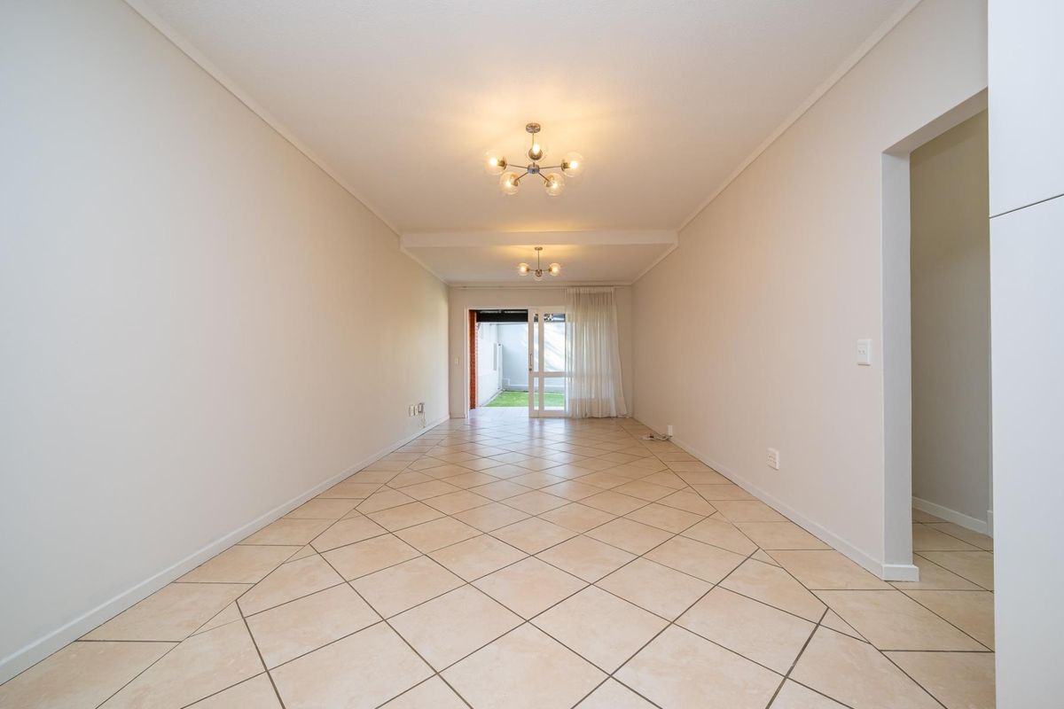 A bright, empty living area featuring neutral tiled flooring, coved ceilings, and a sliding glass door providing access to the outdoor space.