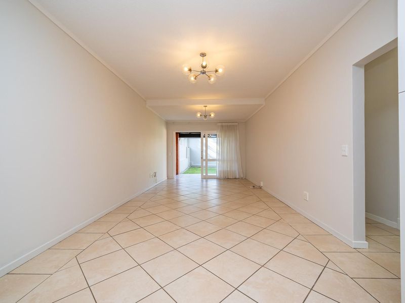 A bright, empty living area featuring neutral tiled flooring, coved ceilings, and a sliding glass door providing access to the outdoor space.