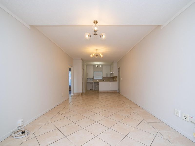 An open-plan living and kitchen area featuring neutral tiled flooring, built-in cabinetry, and functional lighting, offering a clean and versatile space.