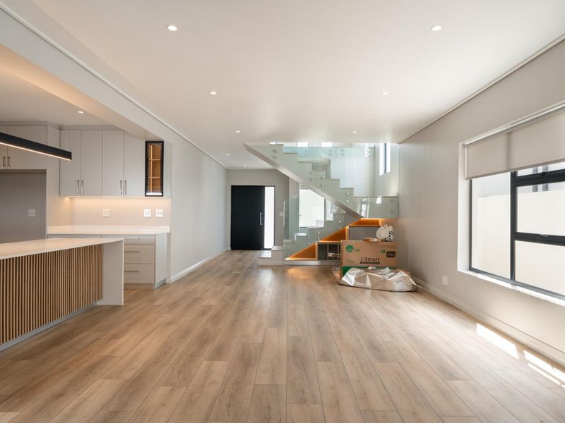 Modern open-plan living area featuring a sleek kitchen with island, light wood-look flooring, and a contemporary staircase with glass balustrades.