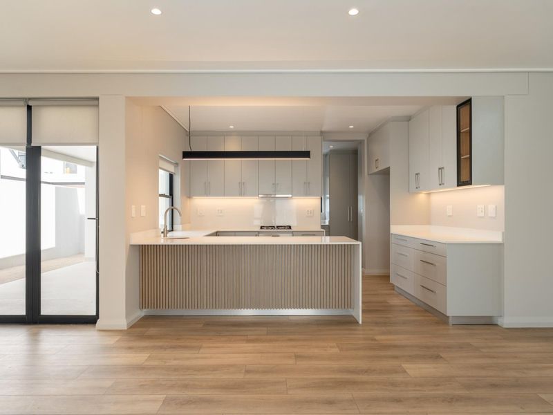 Modern, high-end kitchen featuring sleek cabinetry, quartz countertops, integrated appliances, and a stylish slatted timber island, seamlessly connected to an outdoor patio area.
