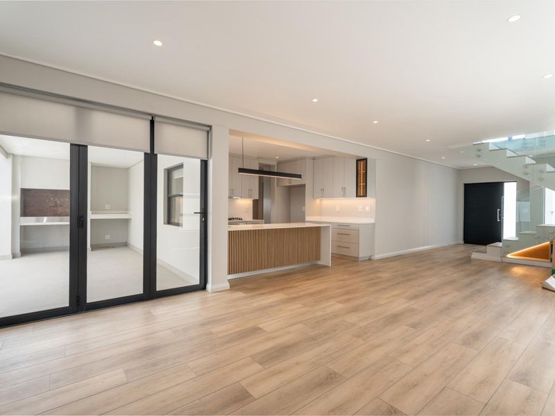 Spacious open-plan living area featuring modern kitchen cabinetry, a central island, laminate flooring, and a contemporary glass staircase.