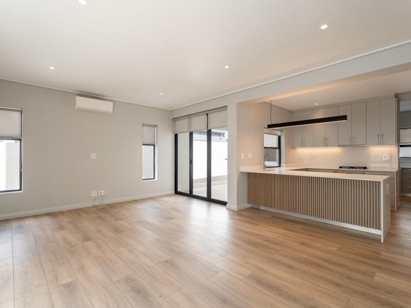 Modern open-plan living area featuring light laminate flooring, recessed lighting, and a contemporary kitchen with stone countertops and slatted timber island detailing.