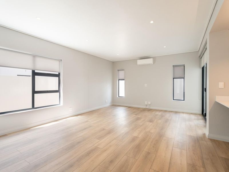 A bright, modern, and spacious living area featuring neutral tones, laminate flooring, recessed lighting, and a wall-mounted air conditioning unit.