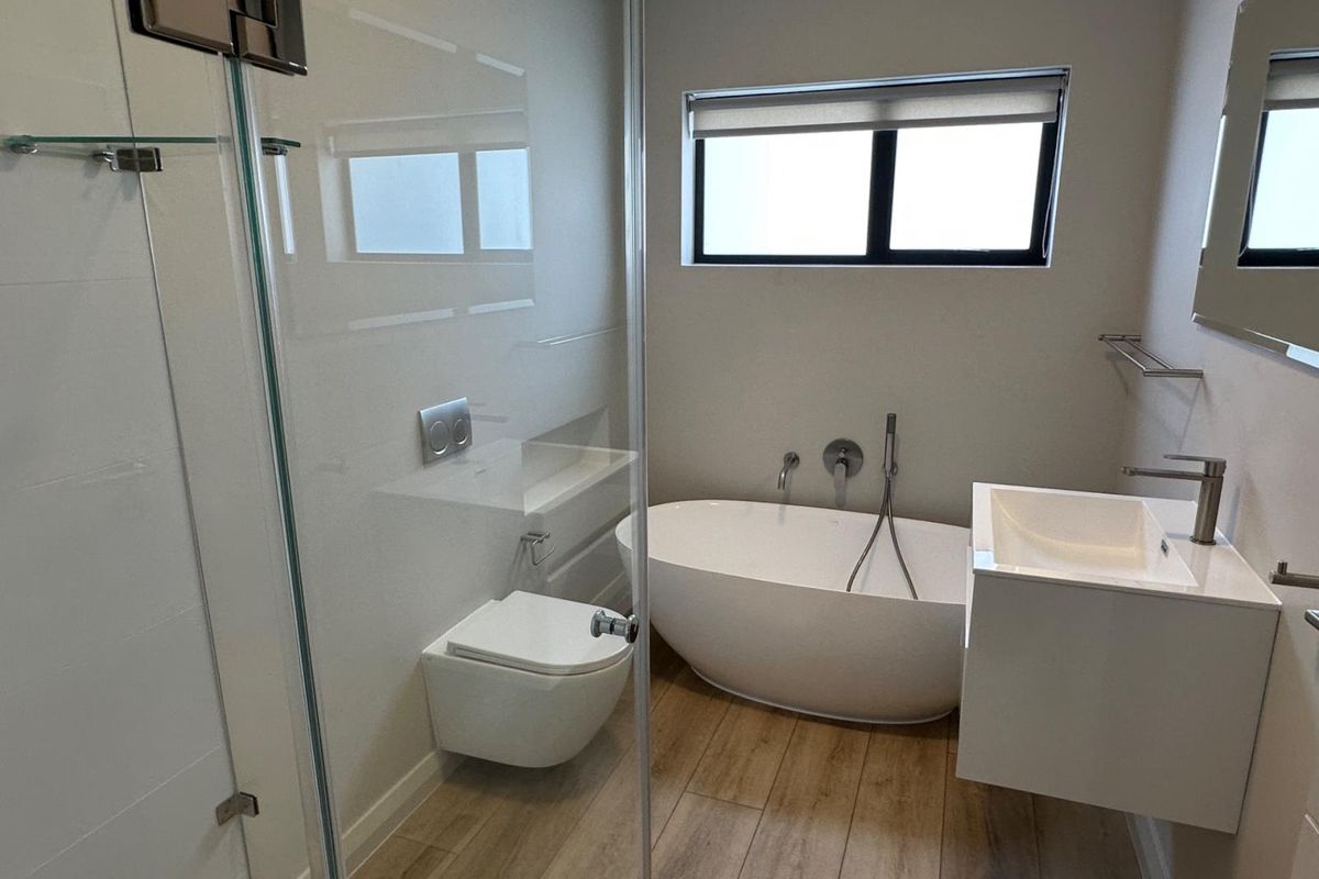 Modern bathroom featuring a sleek freestanding bathtub, wall-mounted toilet, floating vanity, and a glass-enclosed shower with contemporary wood-look tile flooring.