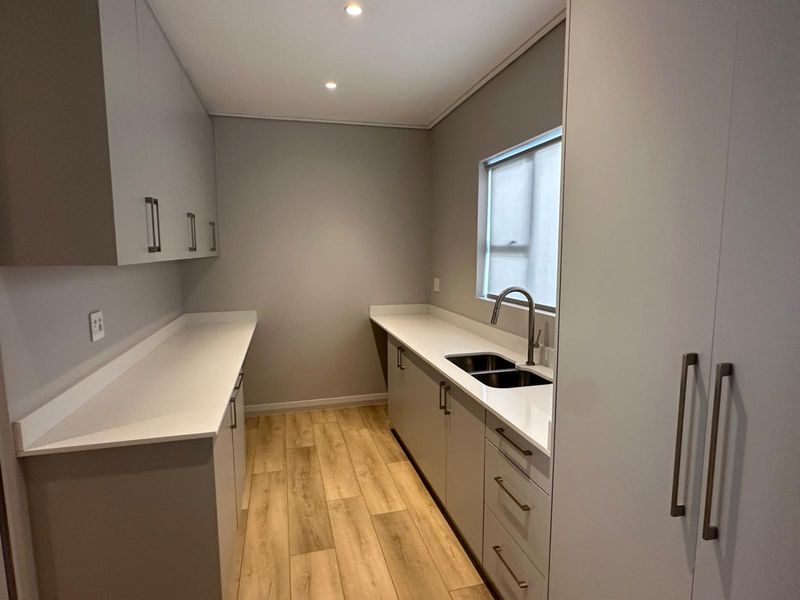 Modern scullery featuring sleek grey cabinetry, white stone countertops, an undermount double sink with a gooseneck faucet, and wood-look tile flooring.