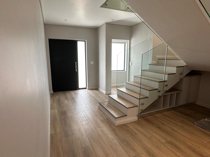 Modern entrance hall featuring a sleek timber staircase with a glass balustrade, integrated under-stair storage, and contemporary laminate flooring.