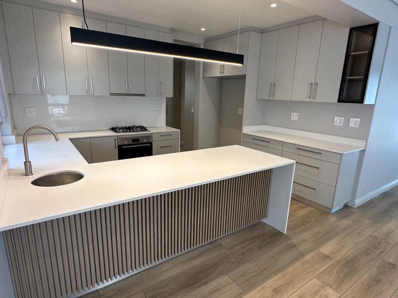 Modern kitchen featuring light grey cabinetry, stone countertops, a central island with slatted timber detailing, and integrated appliances including a gas hob and oven.