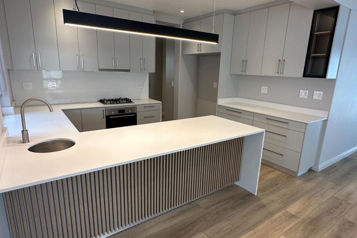 Modern kitchen featuring light grey cabinetry, stone countertops, a central island with slatted timber detailing, and integrated appliances including a gas hob and oven.