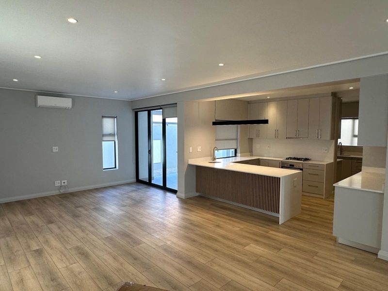 Spacious open-plan living area featuring modern kitchen with stone countertops, built-in appliances, laminate flooring, and seamless access to the outdoor patio through sliding doors.