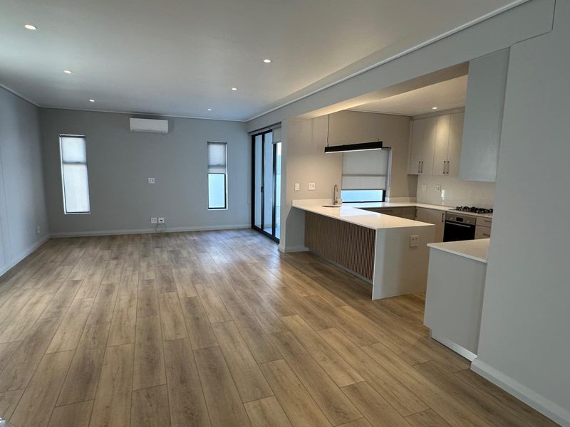 Spacious open-plan living area featuring modern kitchen with island, built-in appliances, and wood-look laminate flooring, leading to a bright, neutral-toned living space.