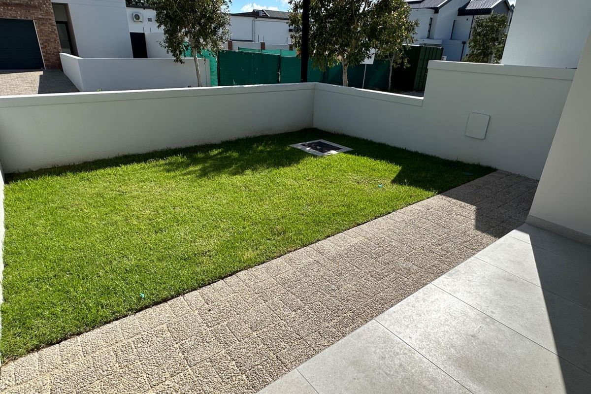 A well-maintained private garden area featuring a neat lawn, paved walkway, and clean boundary walls, offering a tidy outdoor space.