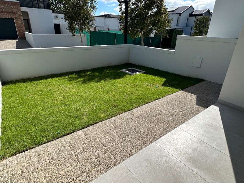 A well-maintained private garden area featuring a neat lawn, paved walkway, and clean boundary walls, offering a tidy outdoor space.