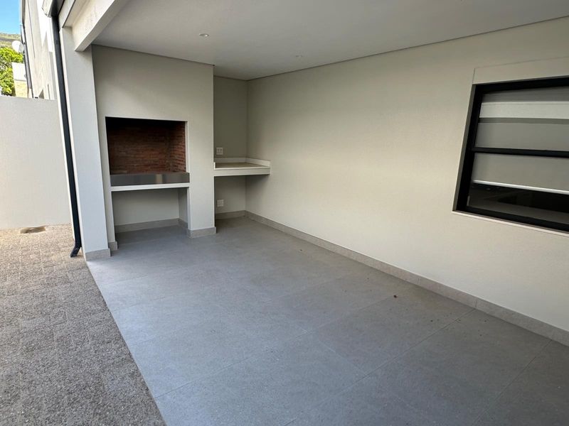 A modern covered patio featuring a built-in braai, stone prep counter, and neutral tiled flooring, offering a clean space for outdoor entertaining.