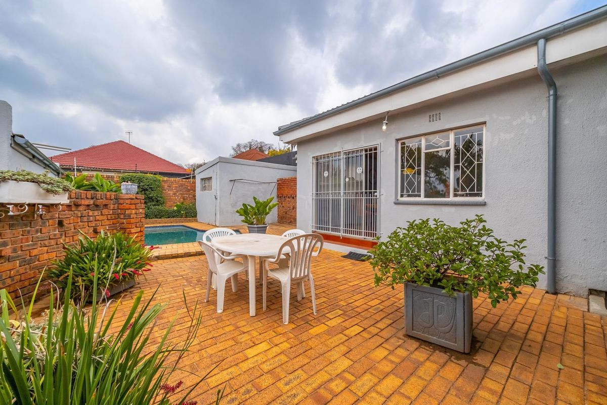 Rear exterior view of the townhouse featuring a brick-paved patio area, a swimming pool, and a secure entrance with security gates and bars.