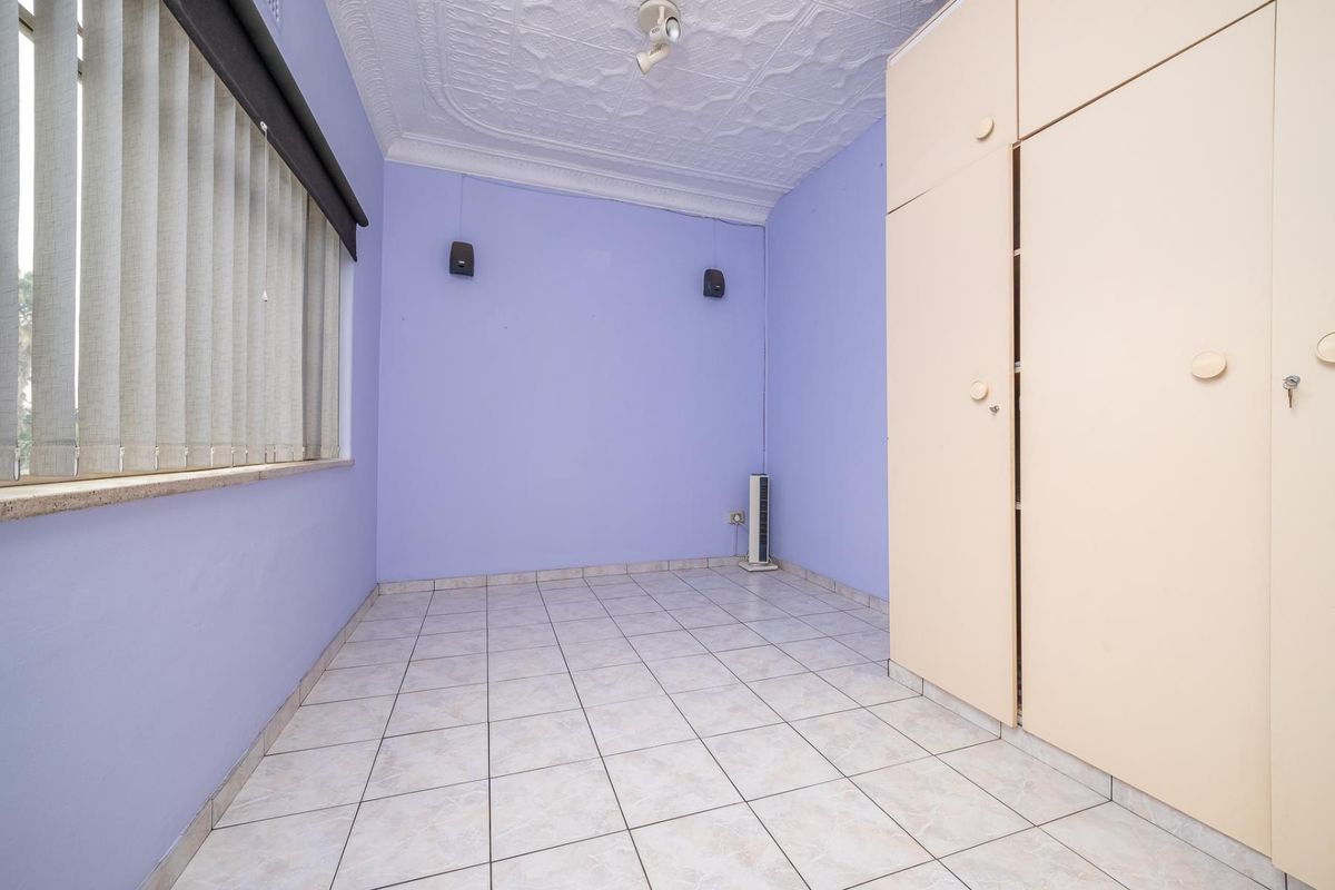 An empty bedroom featuring tiled flooring, built-in cupboards, and an ornate ceiling with coving.
