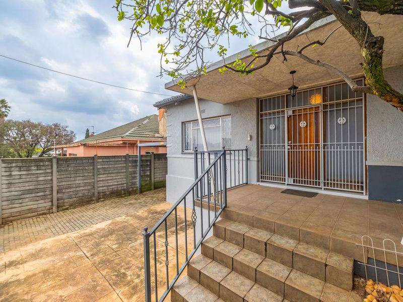 Front entrance of the townhouse featuring a tiled porch, security gate, metal railings, and a paved driveway area.