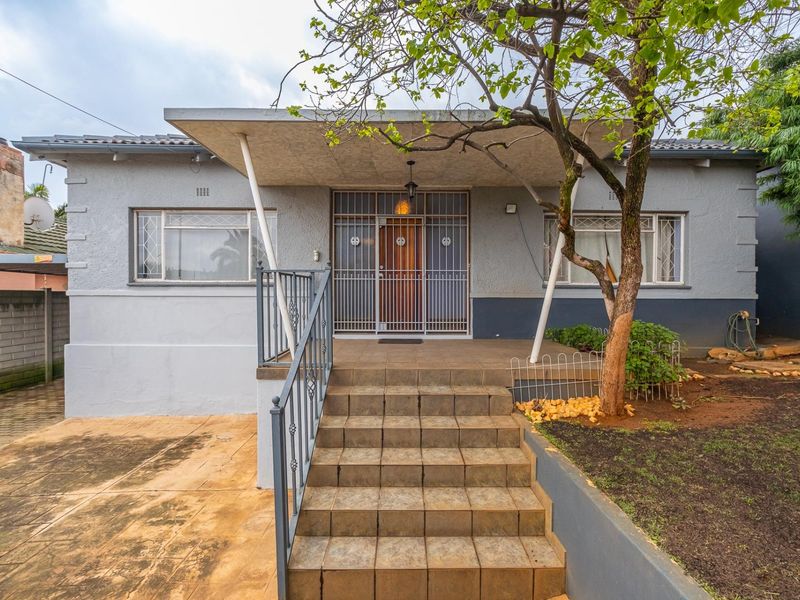 Front elevation of a townhouse featuring a covered porch, tiled entrance steps, metal security gate, and a paved driveway area.
