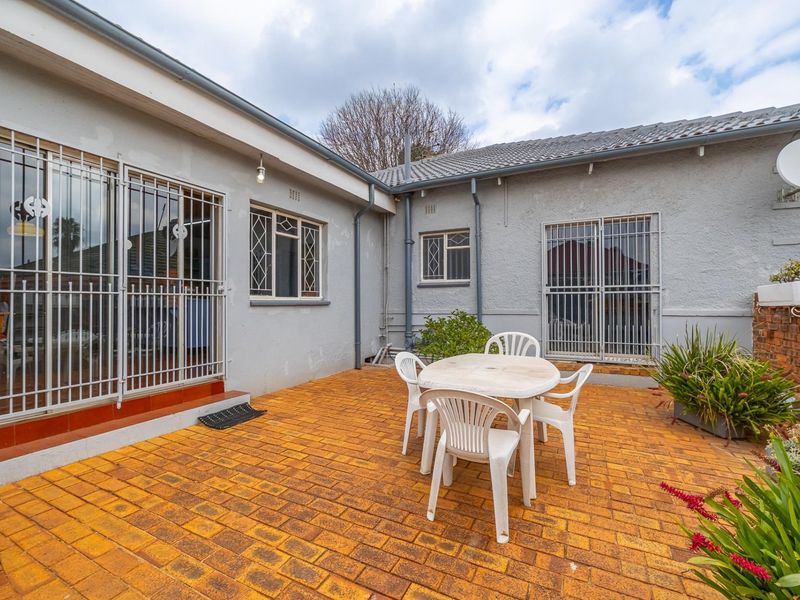 Rear exterior view of the townhouse featuring a brick-paved patio area, security gates on windows and doors, and a tiled roof structure.