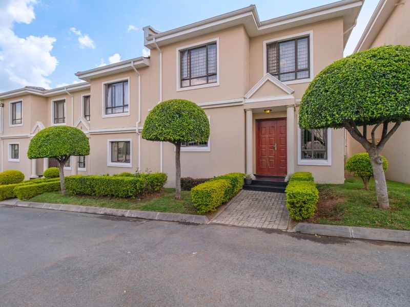 A well-maintained townhouse exterior featuring a paved entrance walkway, manicured garden, and secure window fittings.