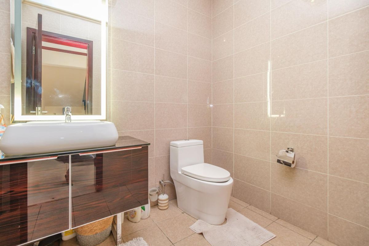 A modern bathroom featuring a sleek vanity cabinet with a vessel sink, a backlit mirror, and full-height wall tiling.