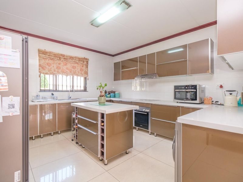 A well-maintained kitchen featuring modern high-gloss cabinetry, a central island, built-in oven, extractor fan, and tiled flooring with ample counter space.