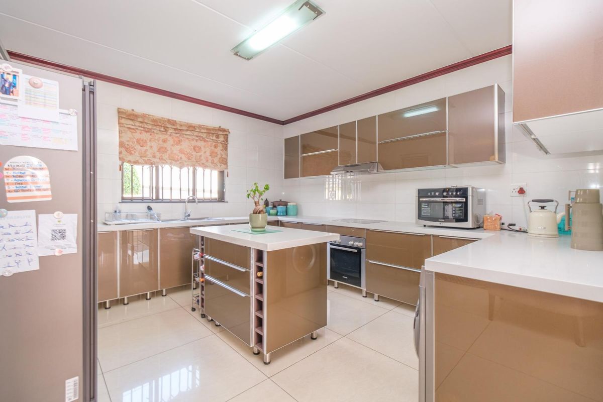 A well-maintained kitchen featuring modern high-gloss cabinetry, a central island, built-in oven, extractor fan, and tiled flooring with ample counter space.
