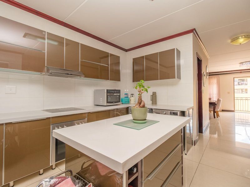 Modern kitchen featuring glossy brown cabinetry, stone countertops, a central island, and integrated appliances, flowing into an open-plan living area.