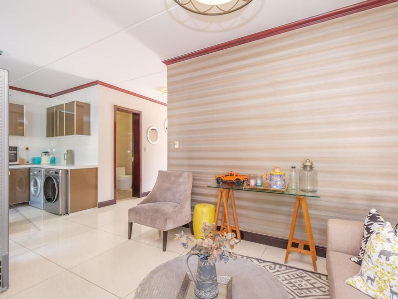 Open plan living area featuring tiled floors, decorative wall finishes, and a compact kitchen space with built-in cabinetry.