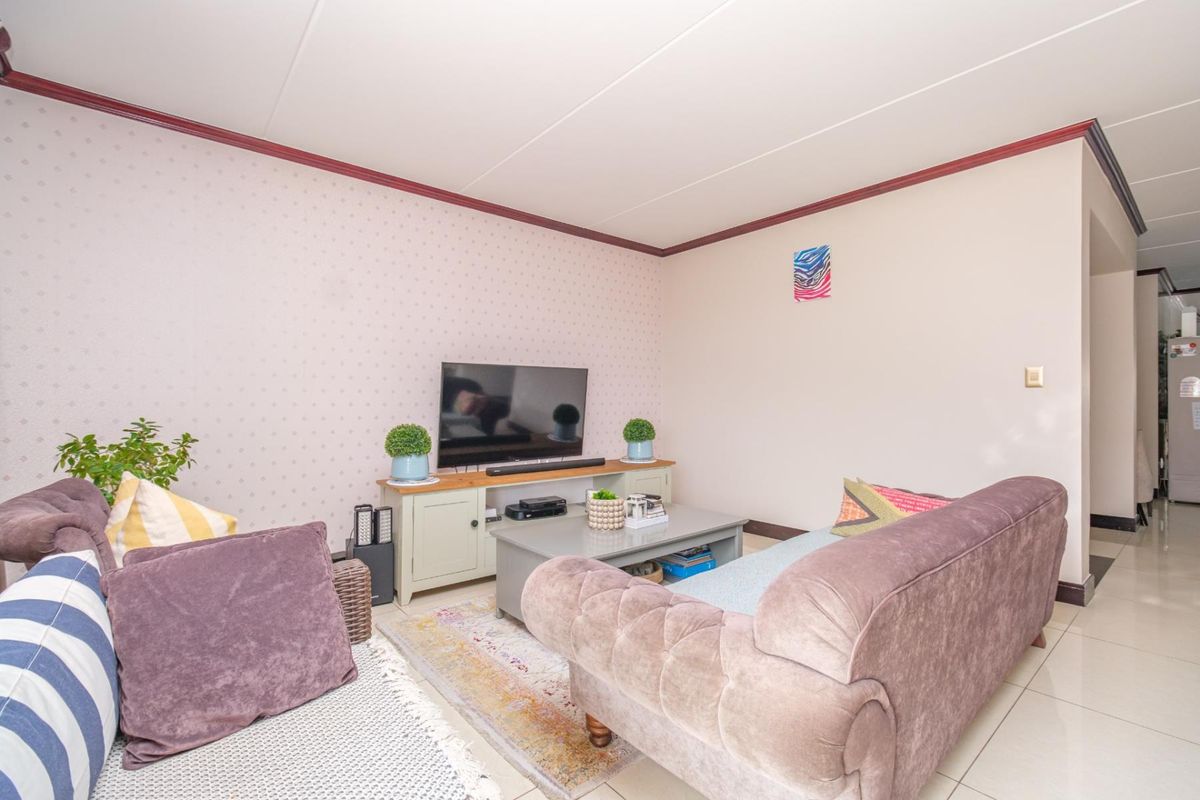 A comfortable living room featuring tiled flooring, decorative coving, and patterned wallpaper, providing a functional and well-lit space for relaxation.