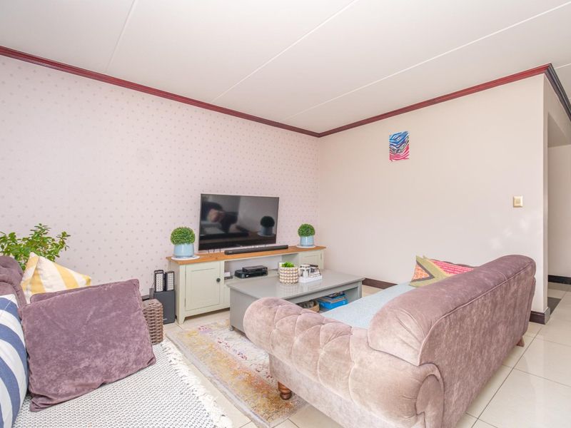 A comfortable living room featuring tiled flooring, decorative coving, and patterned wallpaper, providing a functional and well-lit space for relaxation.