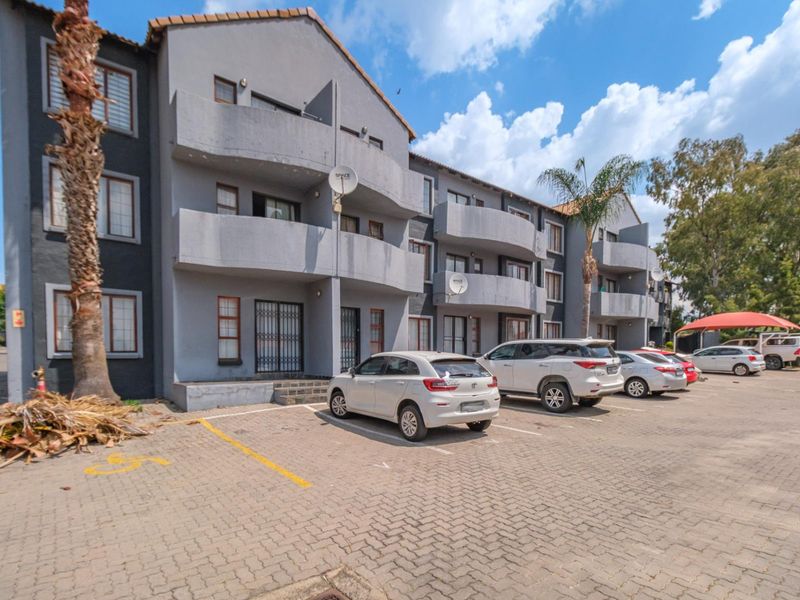 Exterior view of a multi-story apartment complex featuring grey facade, private balconies, and a paved parking area for residents.