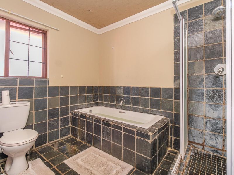 A functional bathroom featuring slate tile finishes, a built-in bathtub, and a separate shower enclosure with a glass door.