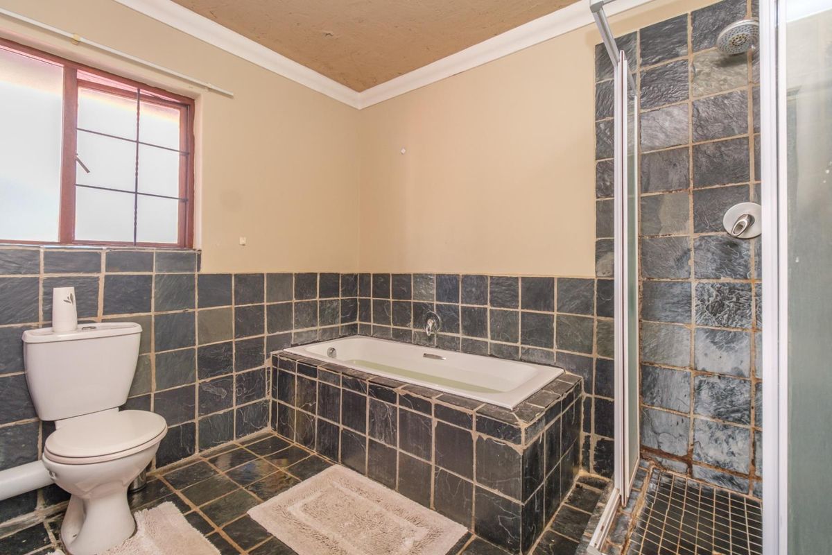 A functional bathroom featuring slate tile finishes, a built-in bathtub, and a separate shower enclosure with a glass door.