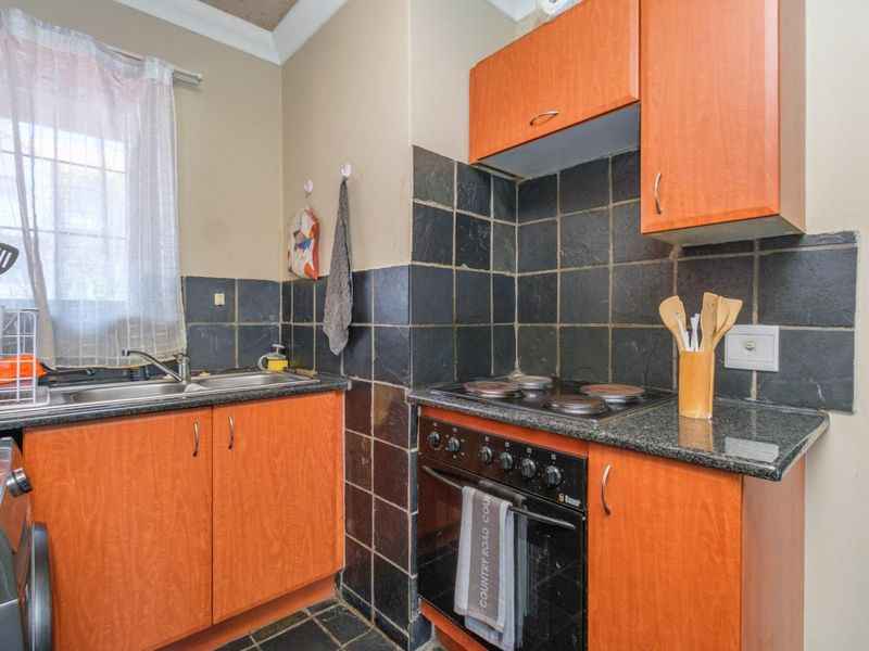 Compact kitchen featuring laminate cabinetry, granite countertops, a built-in oven with electric hob, and dark tiled backsplash and flooring.