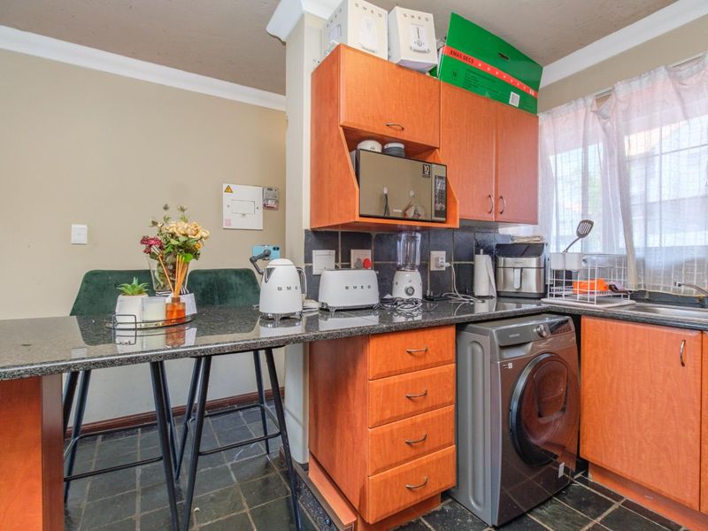 Compact kitchen featuring granite countertops, wooden cabinetry, tiled flooring, and an integrated washing machine, offering a functional layout for daily use.